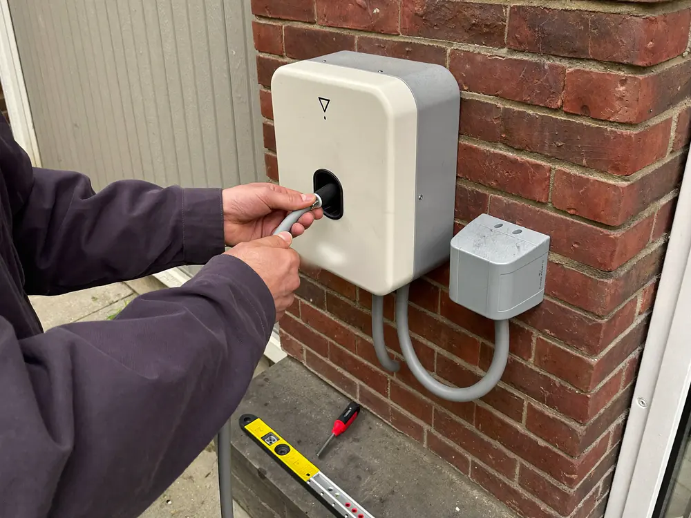 Elektricien zet de kabelwartel vast van een witte laadpaal aan een bakstenen garagemuur
