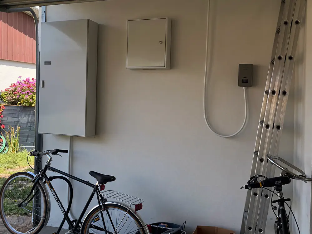 Witte thuisbatterij met een kleine verdeelkast aan de muur van een opgeruimde garage