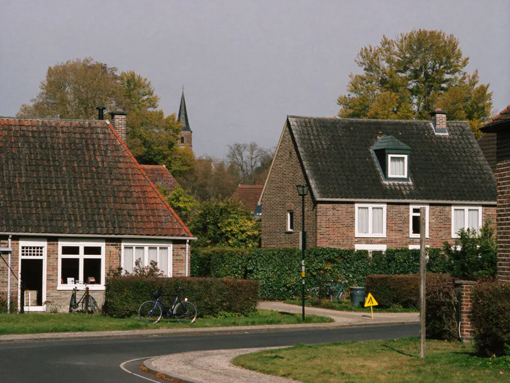Dorpsstraat aan de rand van de Veluwe met bakstenen huizen, hagen, fietsen en een kerktoren in de verte